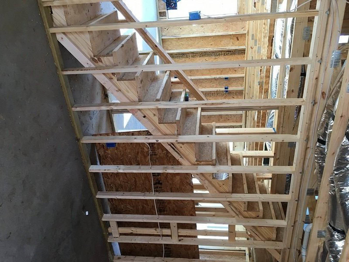 Exposed wooden framing and beams in a house under construction, wooden staircase, ladder leaning against wall, blue basket on ledge, silver foil-wrapped insulation