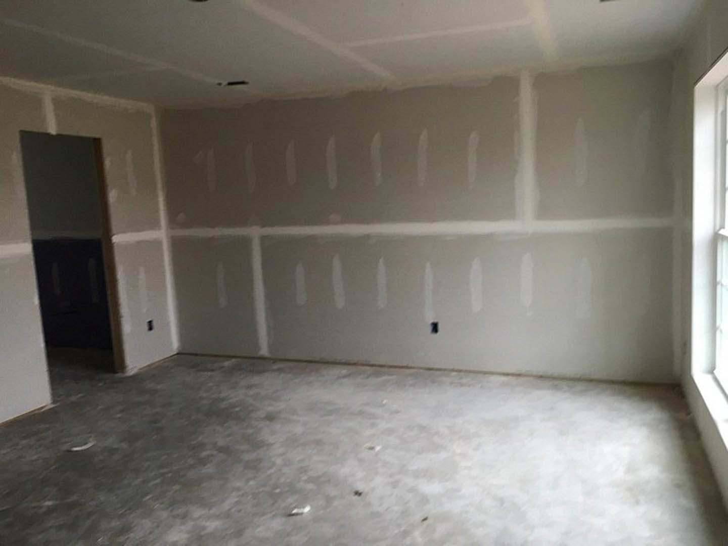 White-painted walls, concrete tile flooring, white ceiling with central seam, doorway and window visible in minimalist interior.