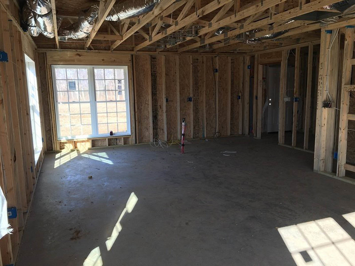 Sunlit room with exposed wooden ceiling beams, white walls, large window, and polished concrete floor