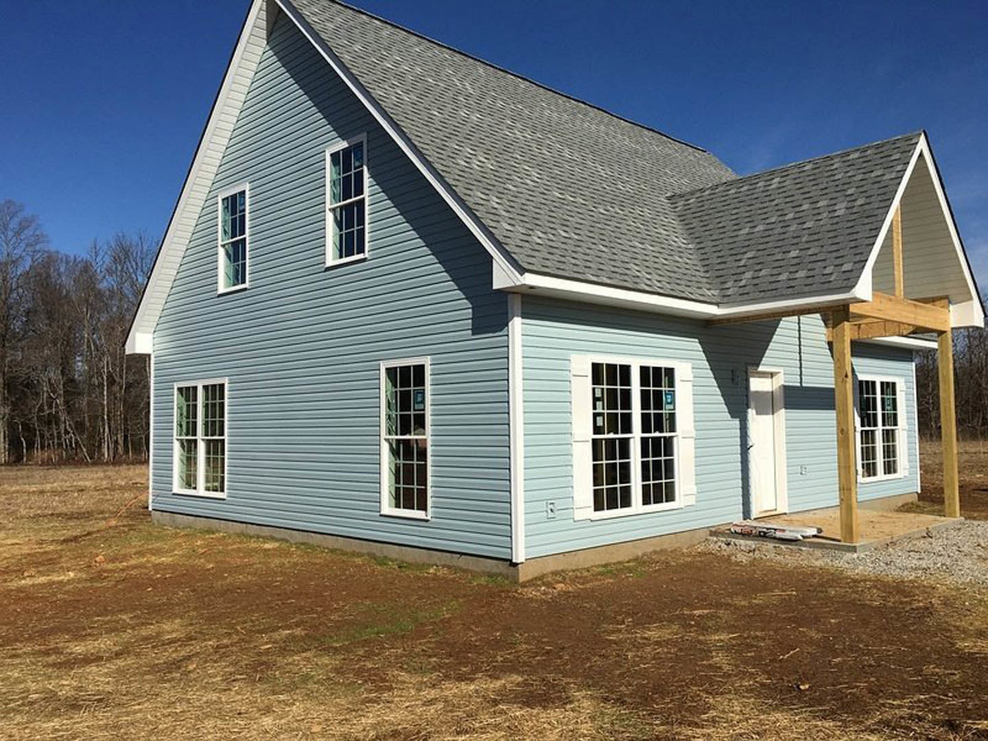 White multi-pane window with white frame set in unfinished siding, bright blue sky above, trees visible in background
