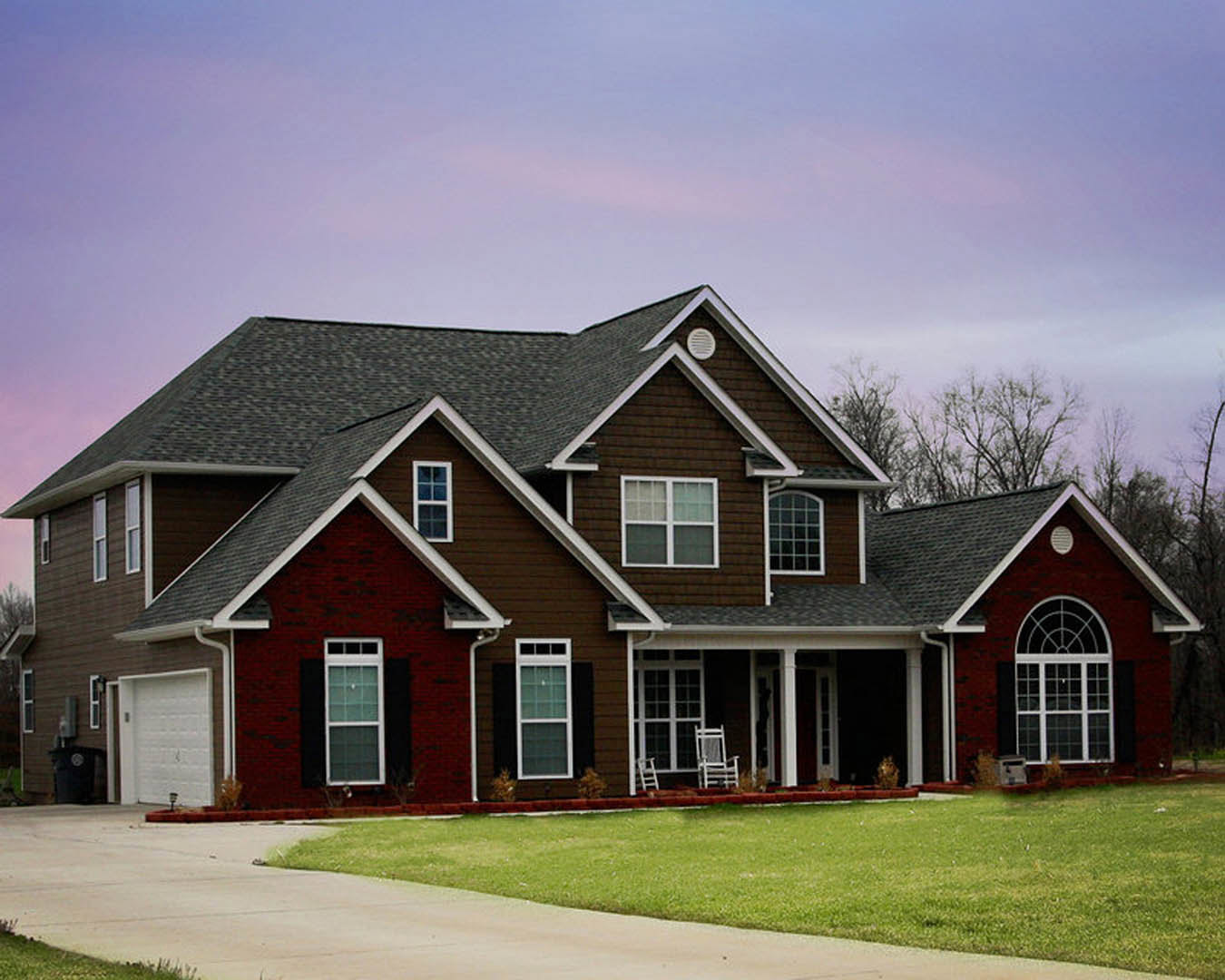 Two-story house with white siding, covered front porch, large windows with glass panes, white garage door, manicured green lawn, and concrete sidewalk.