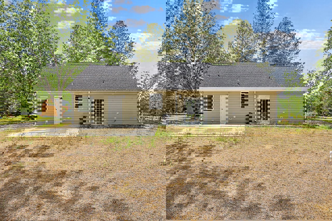 Two-story house with white siding, black-framed windows, concrete driveway, grassy yard, mature trees in the background, and a white front door with black handles.