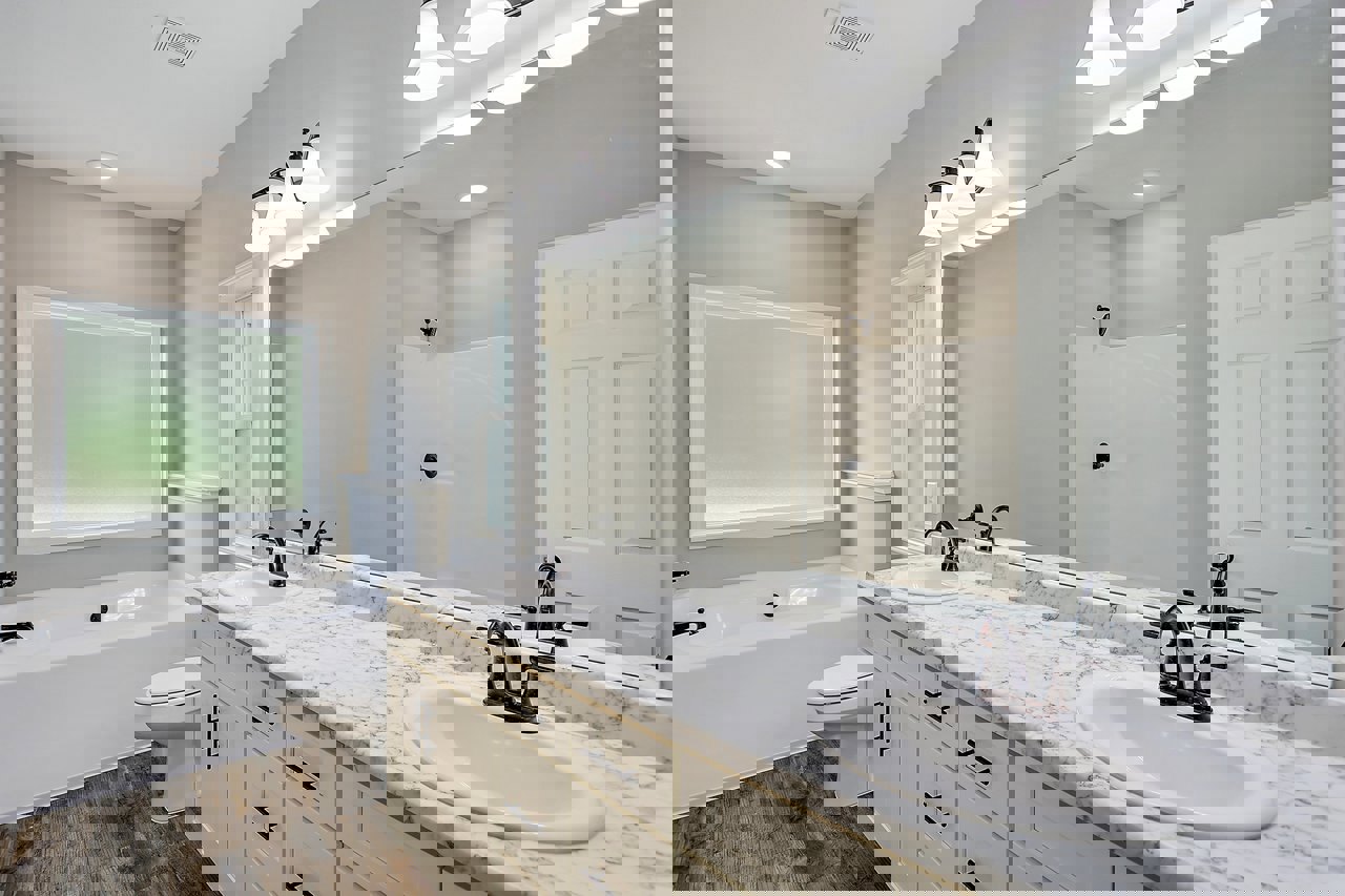 Bathroom featuring marble countertop, freestanding bathtub, frosted glass window, white door with cross design, white sink with black metal bar, closed toilet seat, and four-light