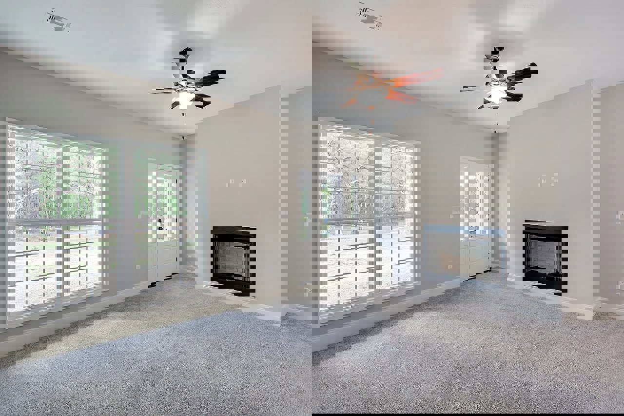 Living room with multi-pane window, ceiling fan with light, glass door fireplace, white door with glass panes, carpeted floor