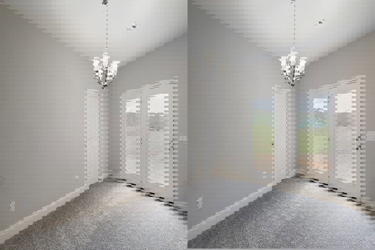 Carpeted room with white paneled door, silver handle, and five-light chandelier with white lamps; plaster walls, crown molding, and view through door to grassy field.