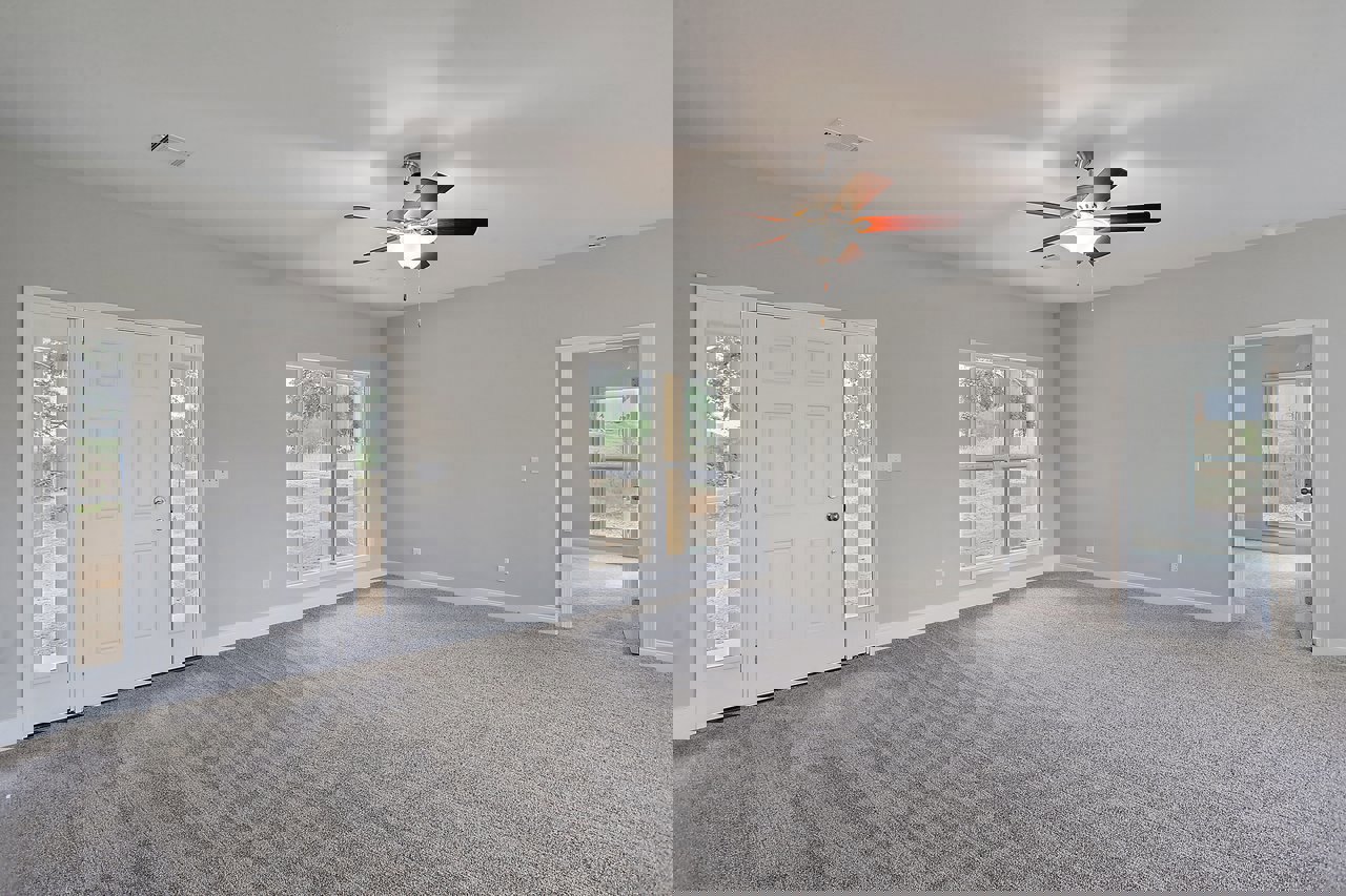 Carpeted room with white paneled door featuring glass windows, ceiling fan with light fixture, and large window overlooking grassy field