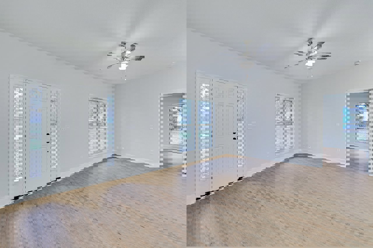 Ceiling fan with light fixture above wood laminate flooring, white door with glass panels, window showing view of neighboring house and trees, plaster walls and ceiling.