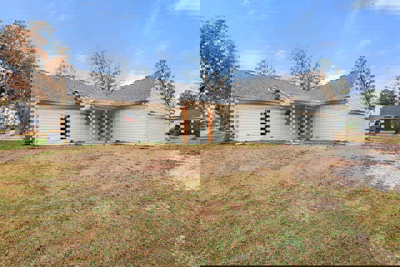 Two-story house with gray siding, covered front porch, dirt patch yard, and a tree with orange leaves in autumn