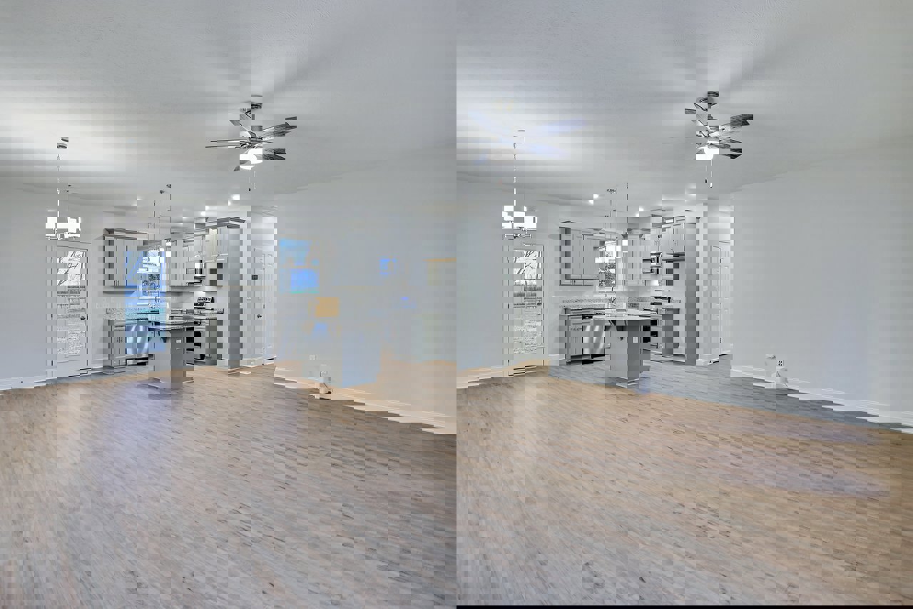 Spacious open floor plan featuring hardwood flooring, a marble-topped kitchen island, ceiling fan with light, and a door overlooking a snowy field