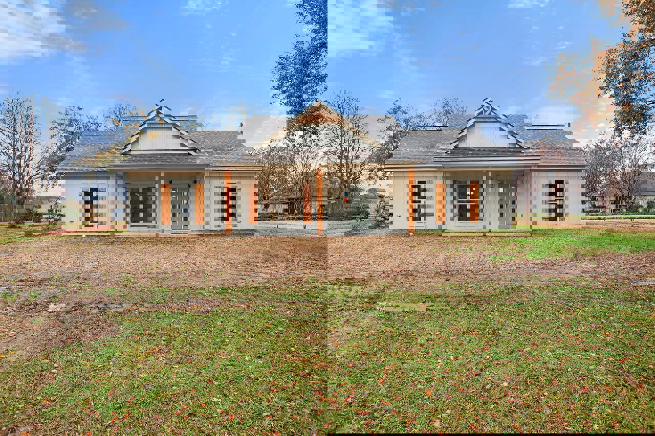 Two-story house with white siding, green front door, grey door with glass panes, white-framed windows, grass lawn, leafless tree, and covered porch under a cloudy sky