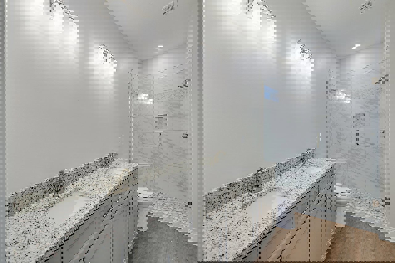 Bathroom with marble countertops, undermount sink, glass-enclosed shower with marble tile walls, white toilet, dark wood cabinetry, and three-light vanity fixture