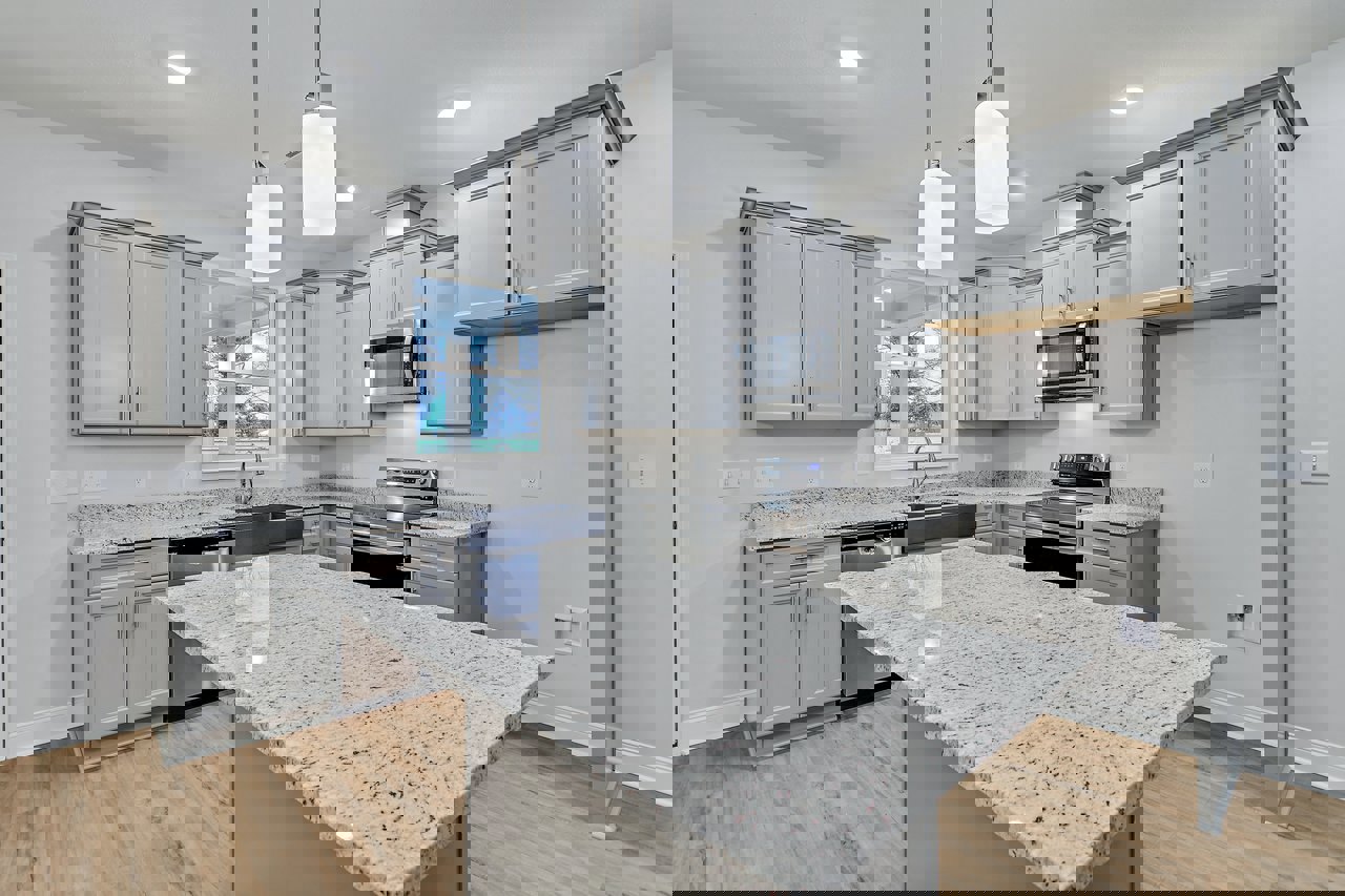 Spacious kitchen featuring a large island with white granite countertop accented by black specks, stainless steel stove, built-in microwave, white cabinetry with grey borders, and