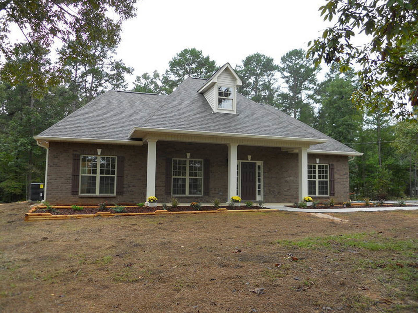 Two-story house with white dormer windows, gray siding, and a covered front porch overlooking a spacious green lawn with mature trees