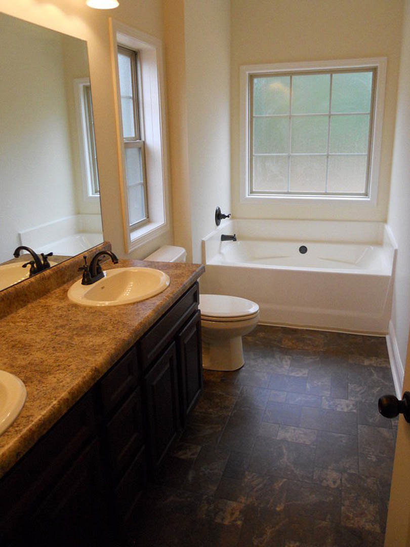 Bathroom with marble countertop, undermount sink, freestanding tub, tile flooring, and large window.