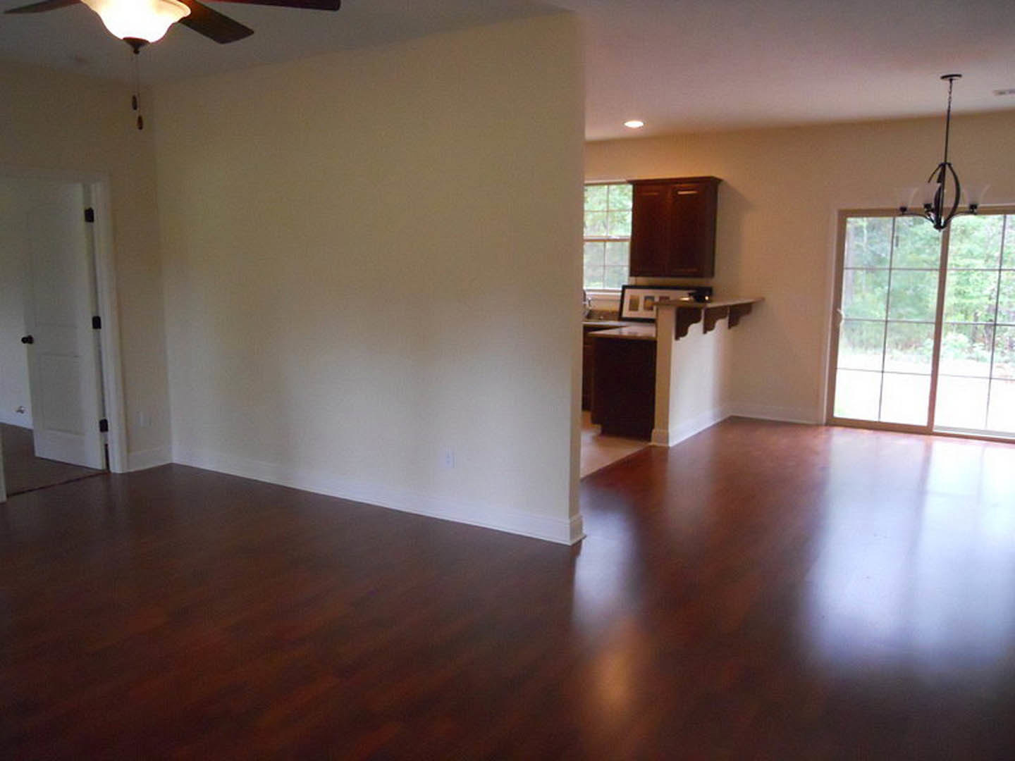 Open kitchen with hardwood floors, white cabinetry, black hardware, ceiling fan, recessed lighting, and large window overlooking outdoor greenery