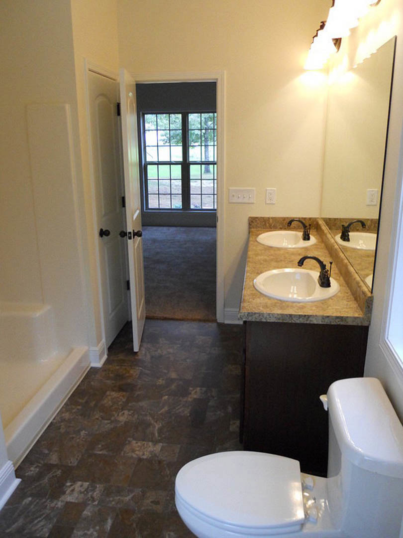 Marble countertop with dual white sinks, black faucets, wall-mounted mirror, white toilet, light tile flooring