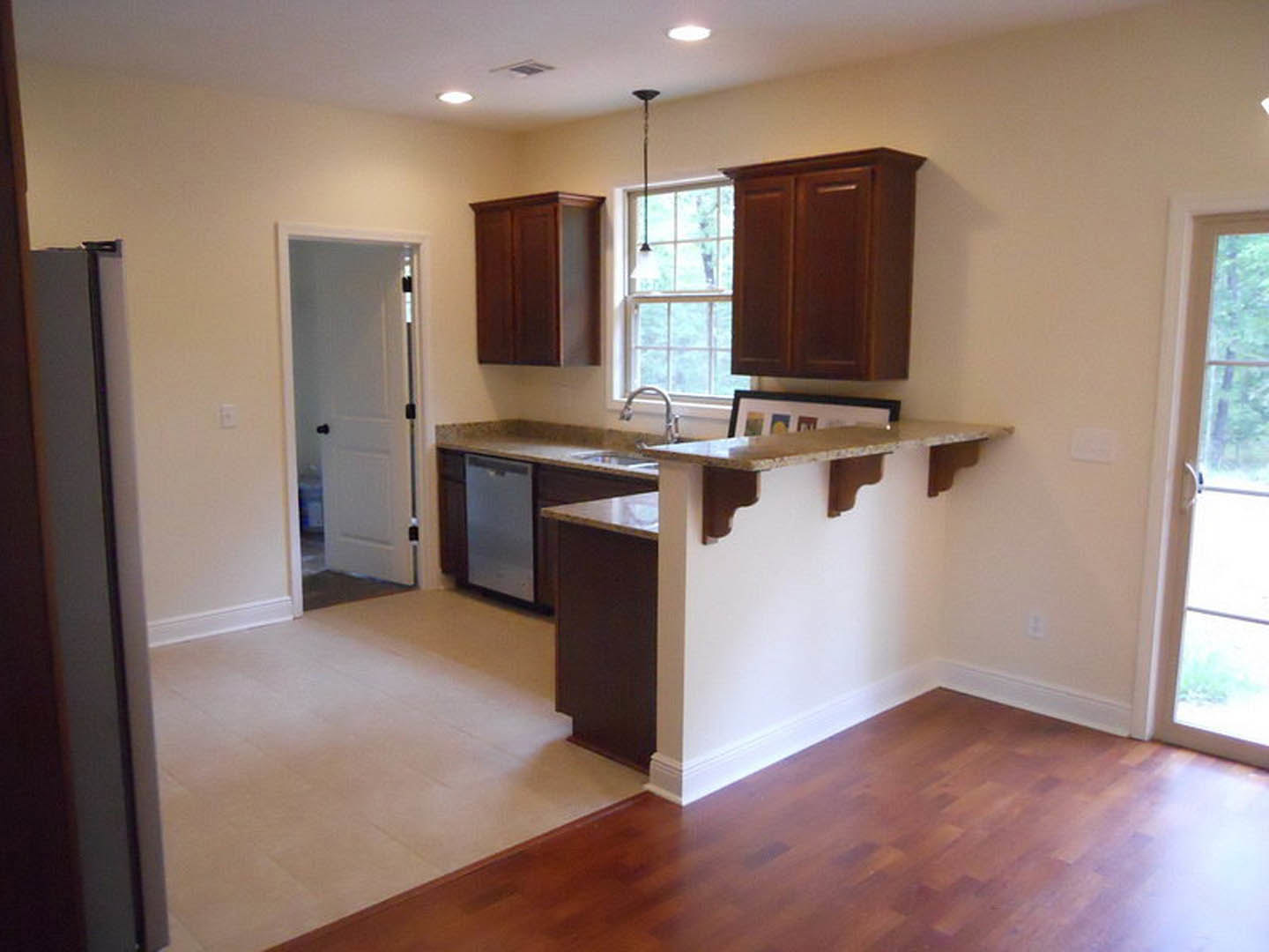 Kitchen with light wood flooring, white cabinetry, black hardware, stone countertop, stainless steel sink, and a white door with black knobs