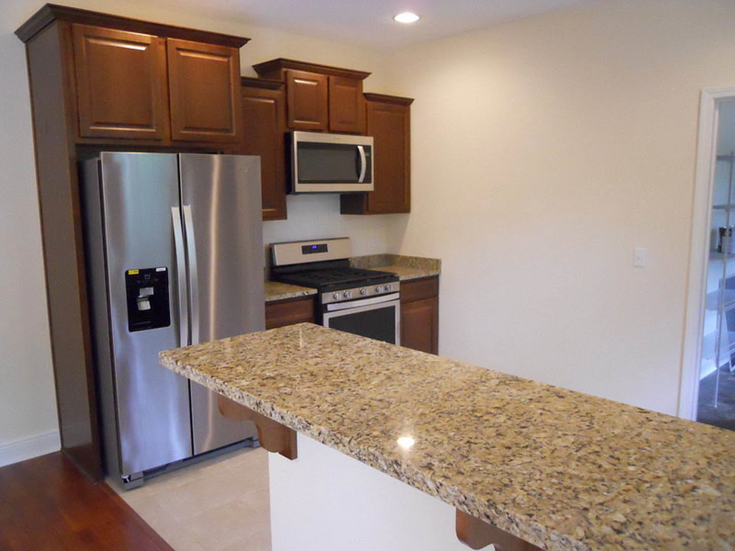 Granite countertops, stainless steel refrigerator, white cabinetry, built-in microwave, electric stove, recessed lighting, neutral tile flooring