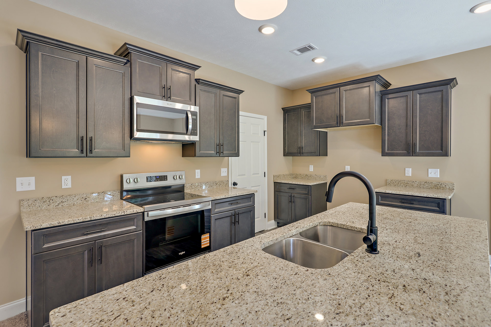 Granite countertops with dark wood cabinets, double stainless steel sink with black faucet, open microwave above stove and oven, neutral tile backsplash