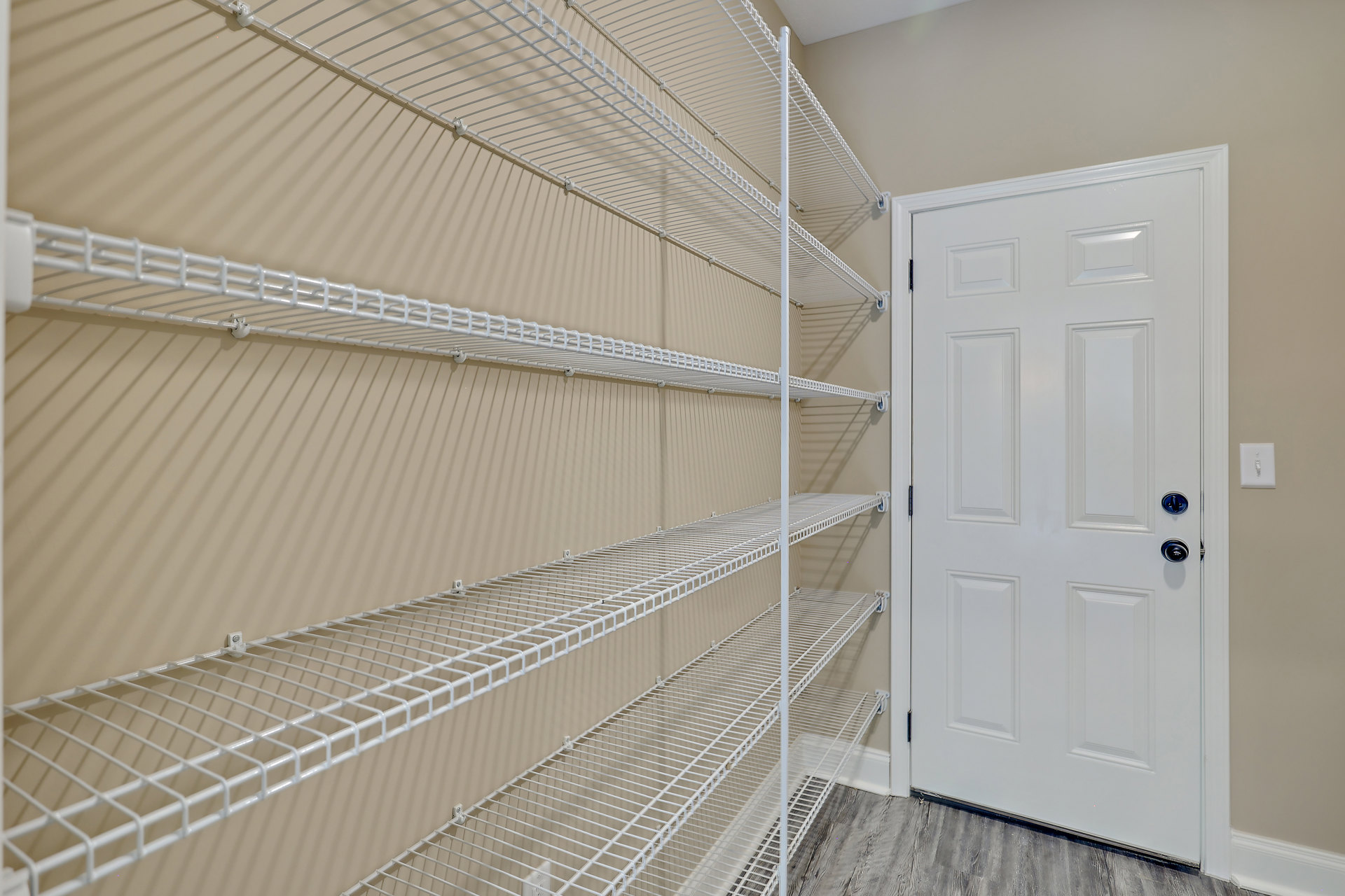 White wire shelves mounted on a wall beside a closed white door with a silver handle and a light switch.