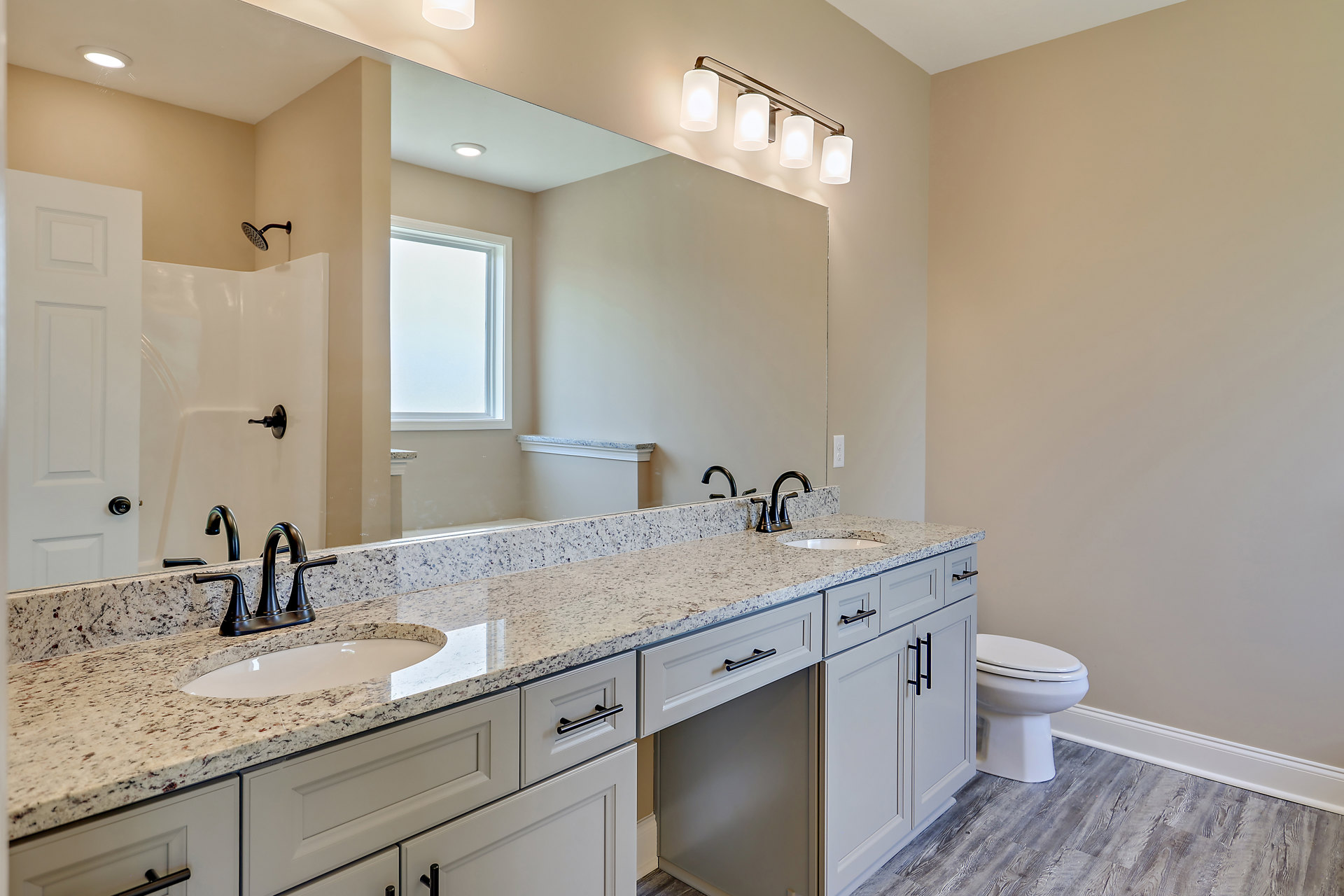 Bathroom with double sinks set in a white countertop, large wall-mounted mirror, white toilet, tiled walls, and modern cabinetry with drawers.