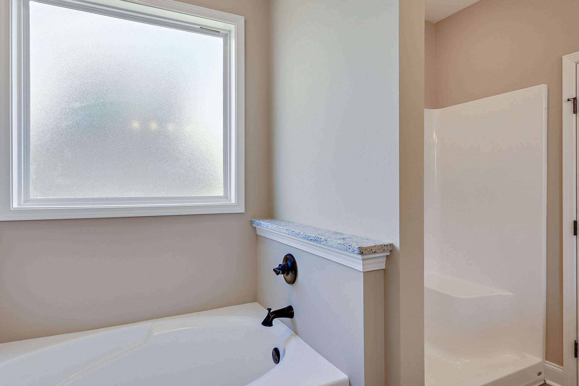 Freestanding white bathtub beneath frosted window with white frame, chrome faucet and wall-mounted switch on smooth white wall