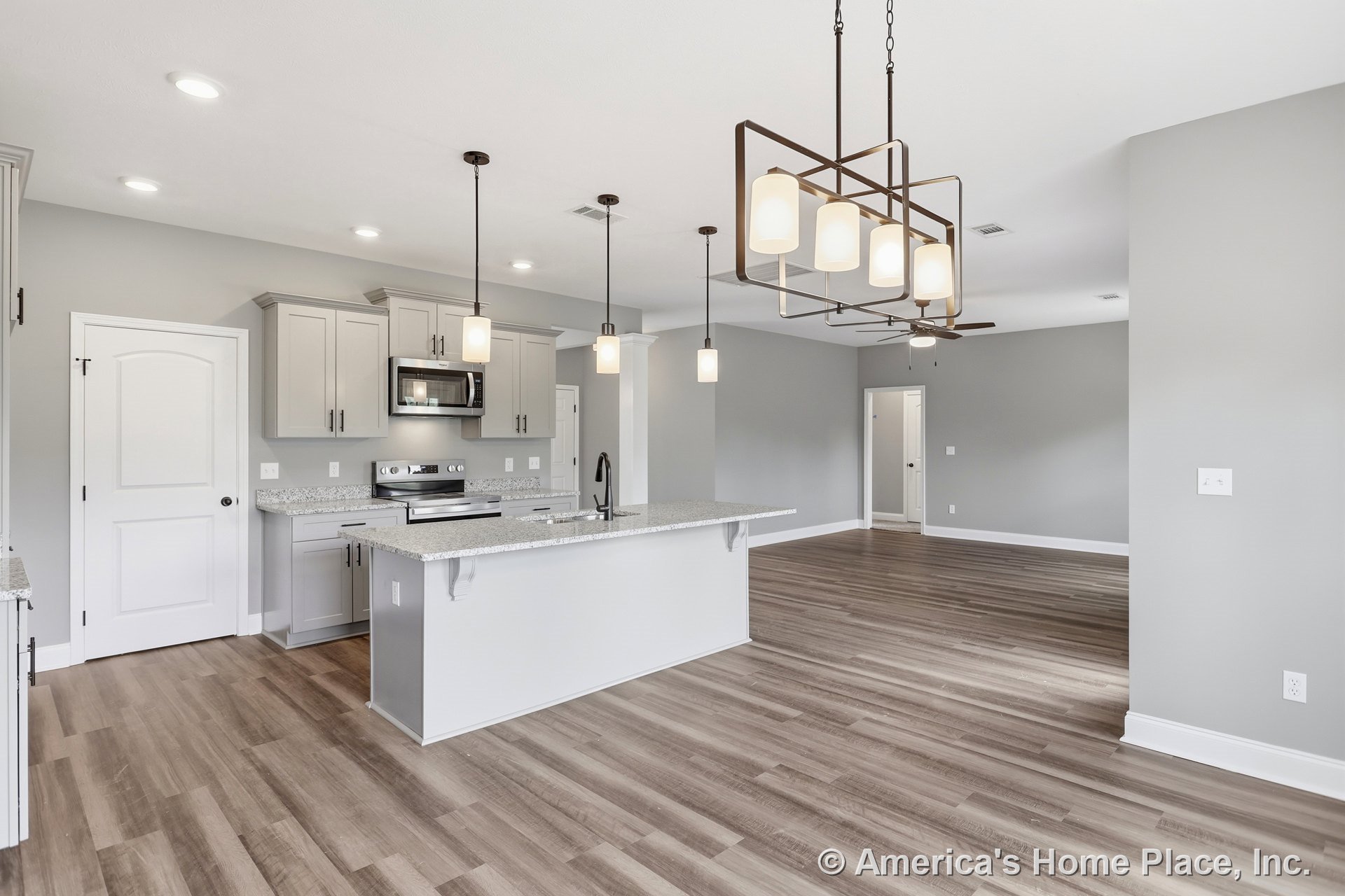 Open kitchen with light gray shaker cabinets, granite countertops, stainless steel appliances, modern pendant and recessed lighting, wide plank wood flooring, and open floor plan.