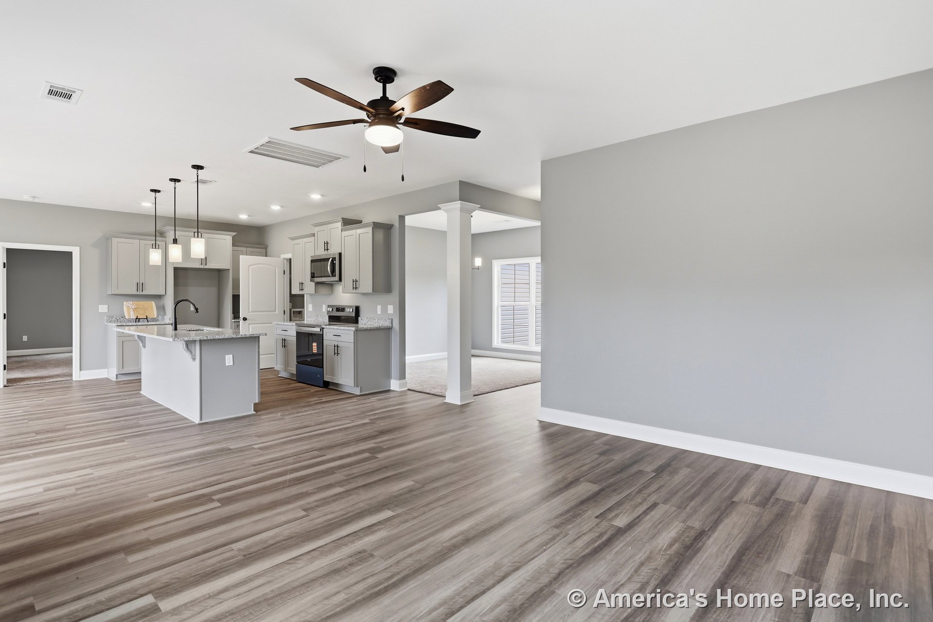 Open-concept kitchen with gray shaker cabinets, granite countertops, pendant lights above island, wood-look vinyl plank flooring, recessed lighting, ceiling fan in adjacent living