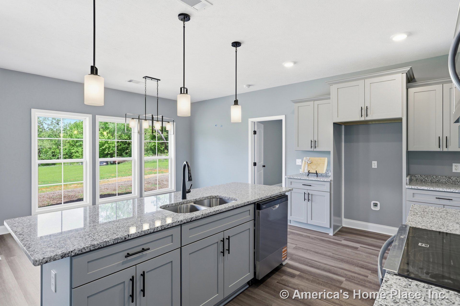 Gray shaker cabinets and granite countertops with a double stainless sink, pendant lights above the island, large windows with white trim, wood-look vinyl flooring, stainless