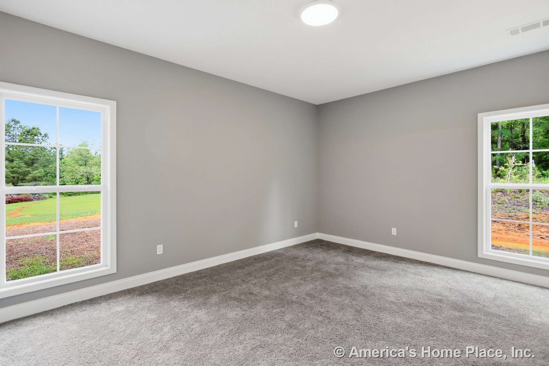 Bedroom with gray carpet flooring, light gray painted walls, two large windows framed in white trim, white baseboards, and a flush ceiling light fixture; natural light fills the
