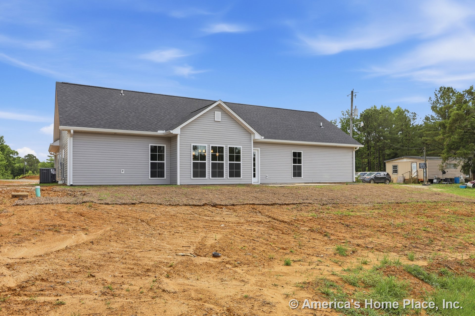 Gray vinyl siding exterior with white trim, gable roof topped with asphalt shingles, multiple large windows, glass-insert back door, and unfinished yard in new single-story