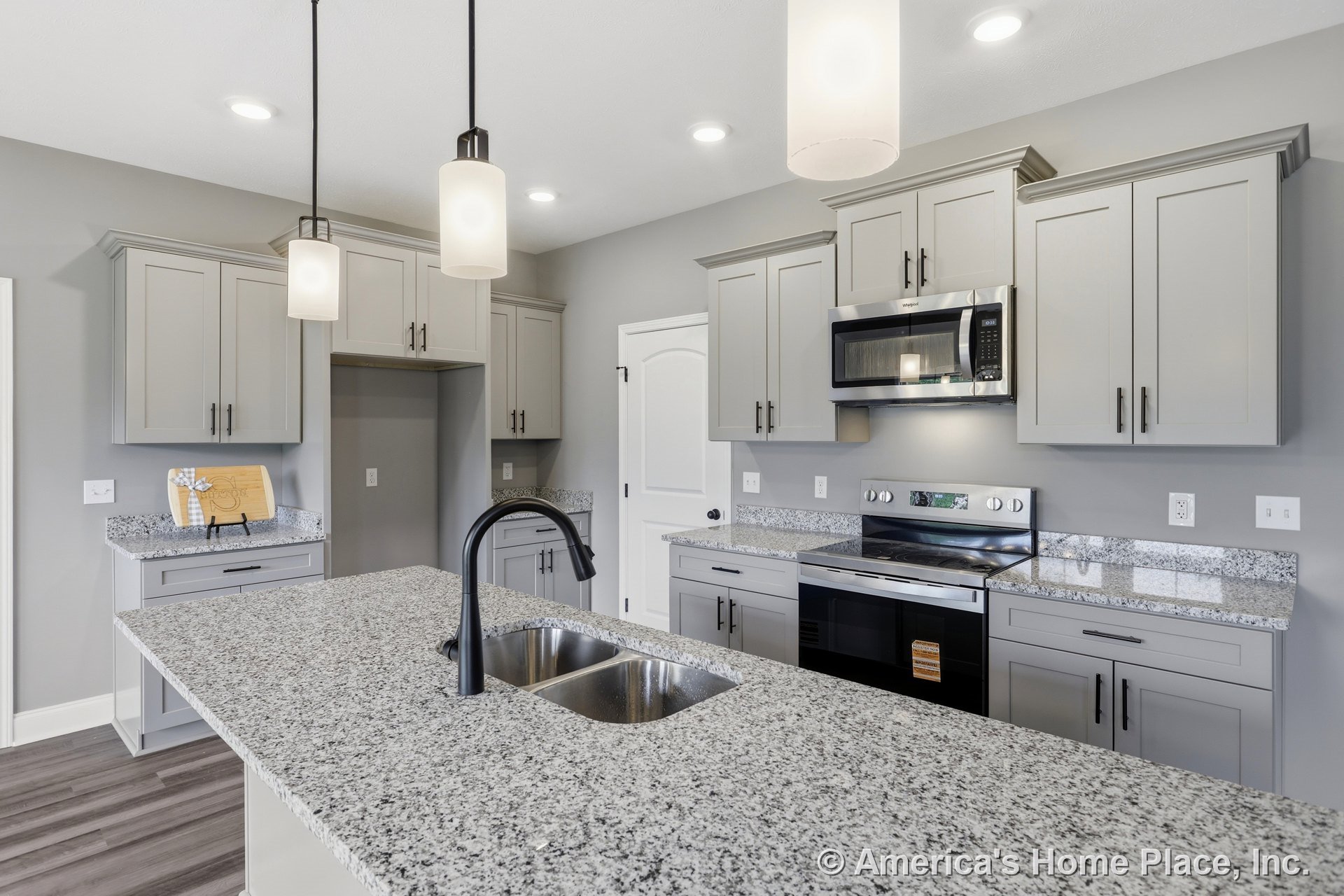Granite island with undermount sink, gray shaker cabinets, stainless steel microwave and oven, pendant and recessed lighting, wood-look flooring, white paneled interior door