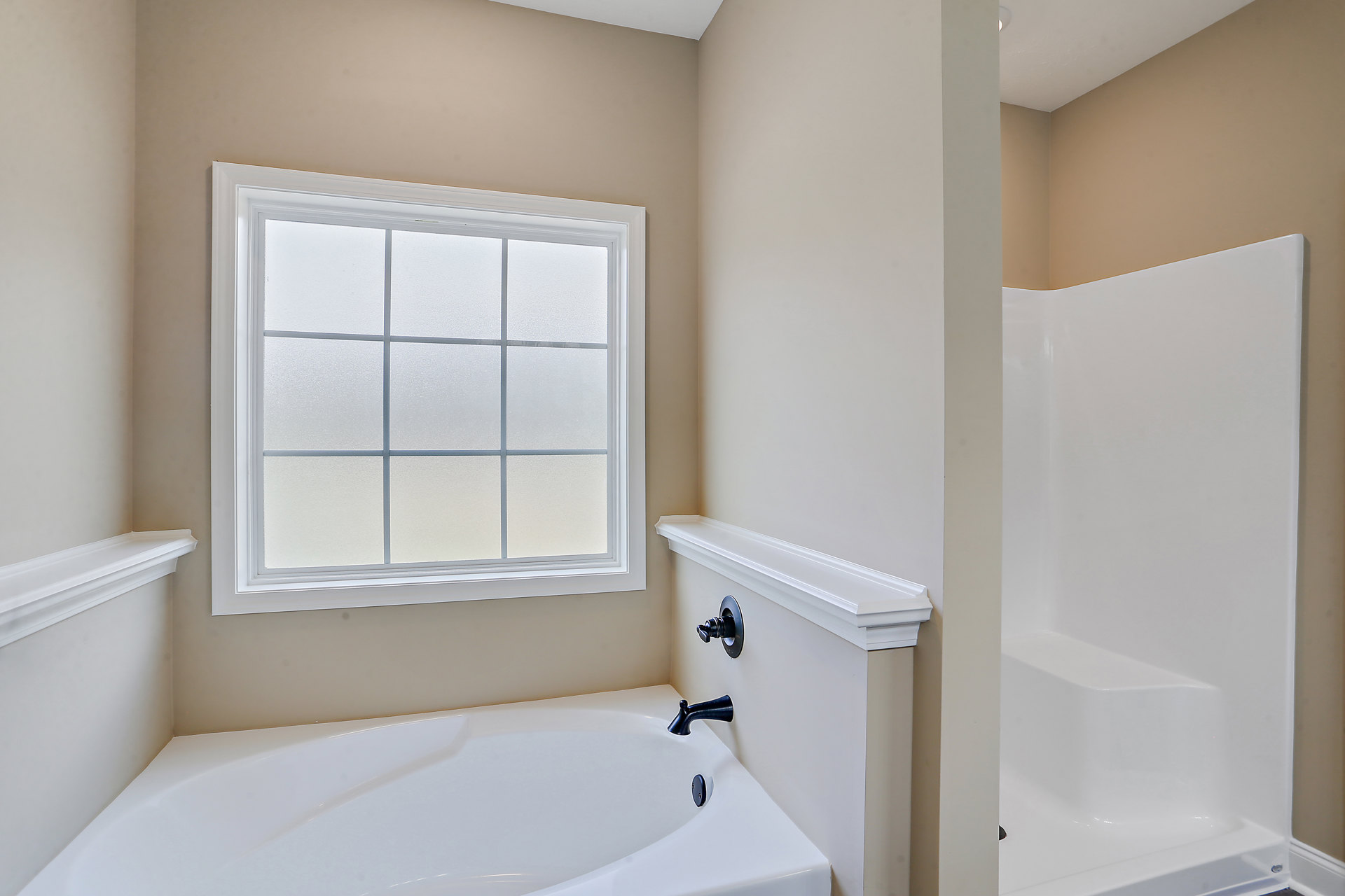 White bathtub with chrome faucet beside glass-enclosed shower, frosted window for privacy, light-colored walls, and modern door hardware.