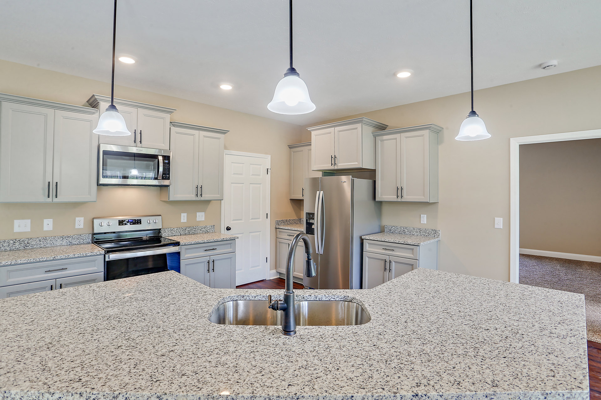 Modern kitchen with stainless steel sink and faucet, white cabinetry, black oven door, built-in microwave with illuminated interior, refrigerator, and stone countertops under