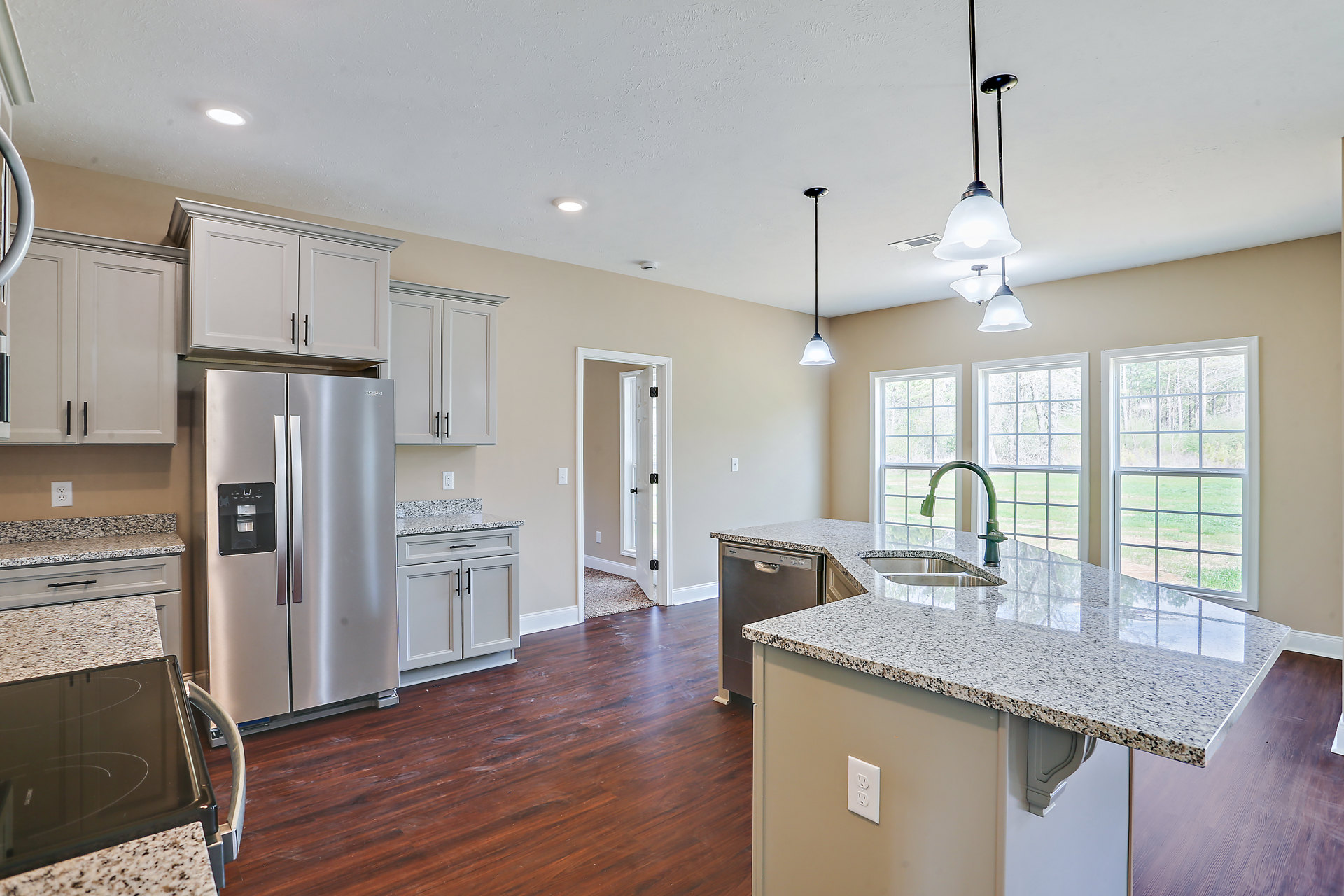 Spacious kitchen featuring a large central island with white quartz countertop, stainless steel refrigerator with black handle, white cabinetry, built-in sink, modern stovetop, and