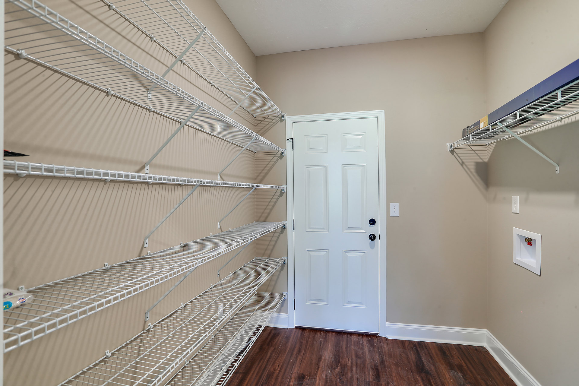 White built-in shelves on a plaster wall, white door with black knobs, wood floor with scattered white specks, white utility box with red valve