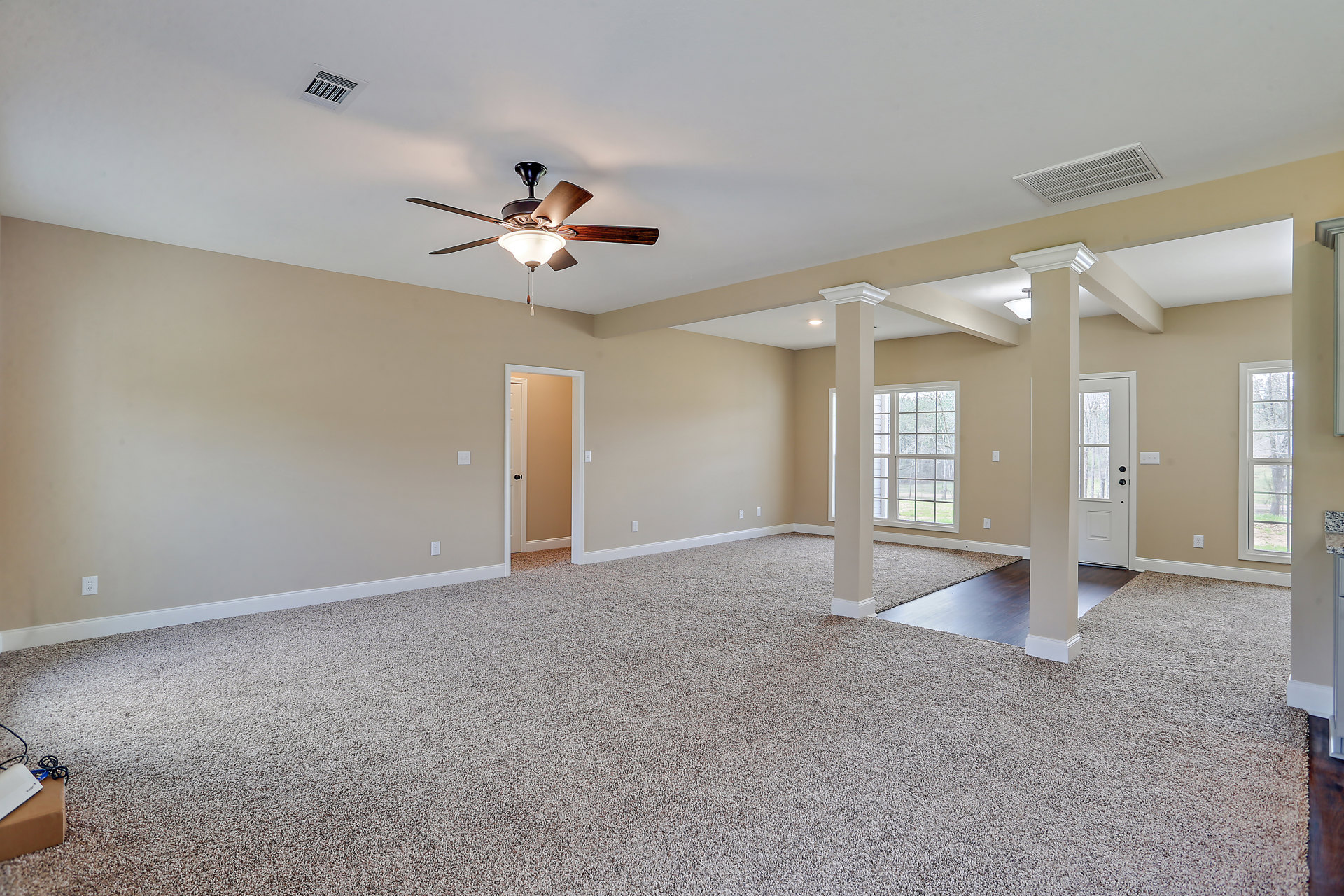 Carpeted bedroom with white walls, ceiling fan with light fixture, large window overlooking leafy tree, ceiling air vent