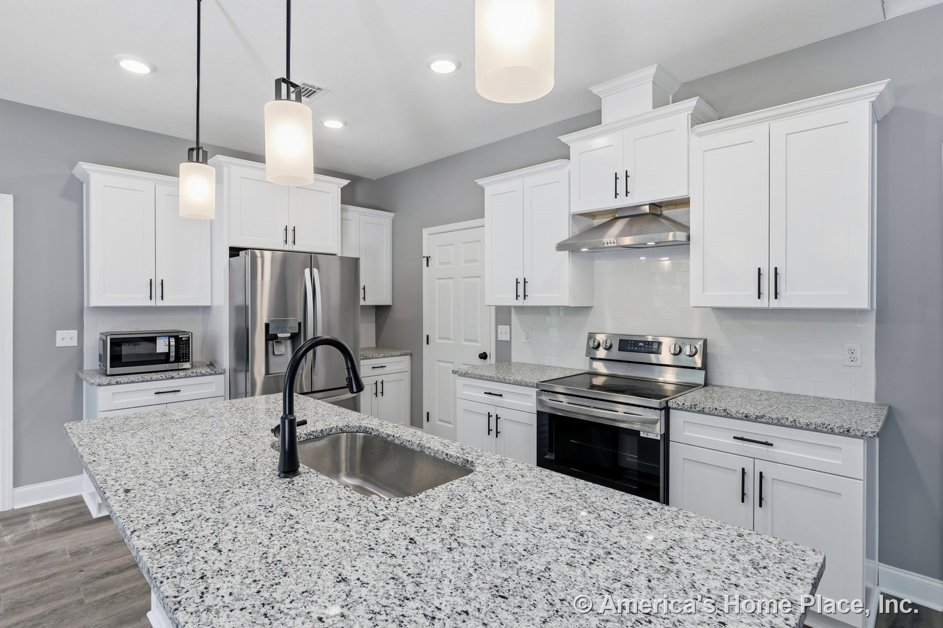 Granite island with undermount sink, white shaker cabinets, stainless steel range and hood, subway tile backsplash, built-in microwave, pendant and recessed lighting, gray painted