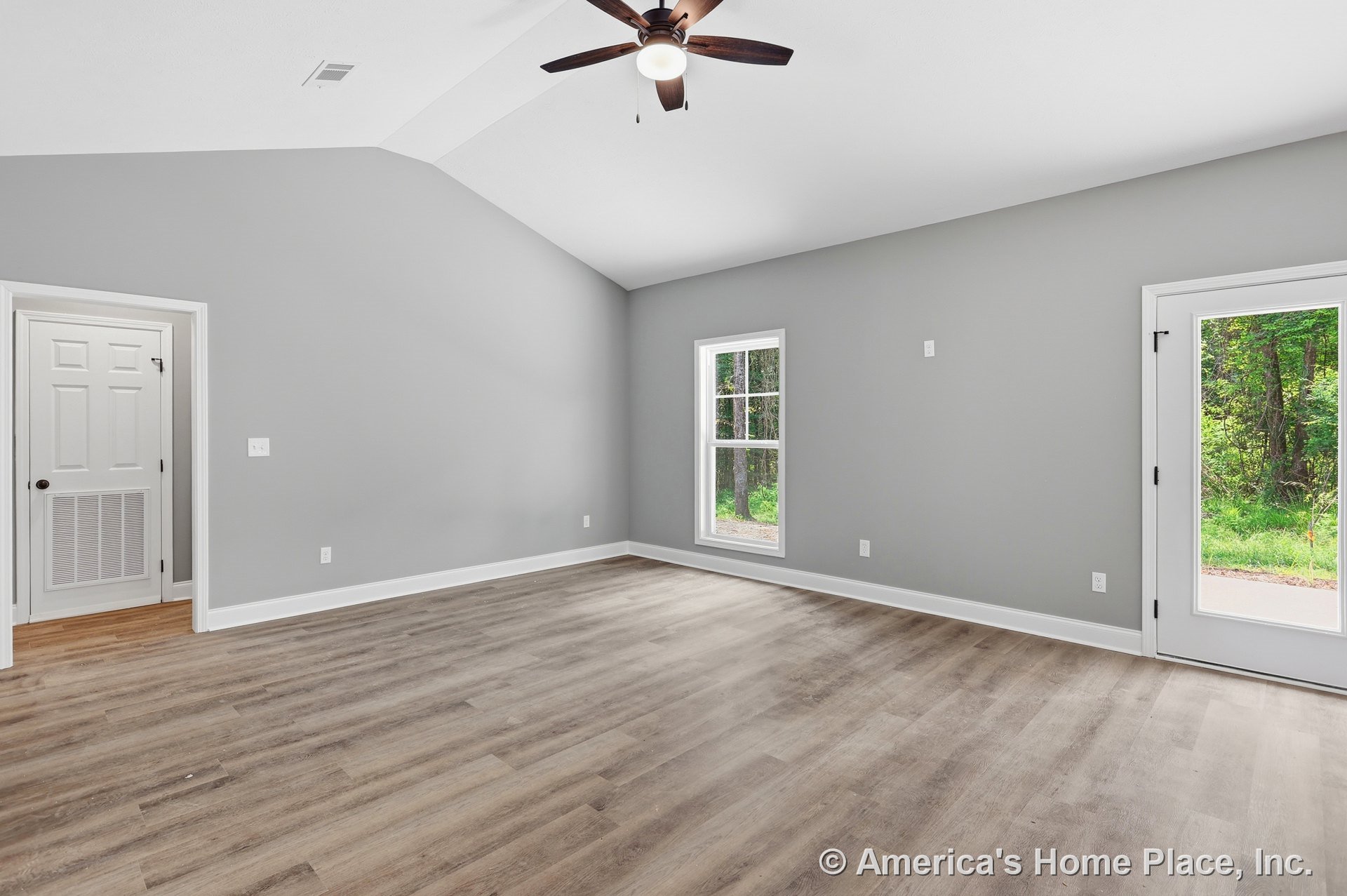 Vaulted ceiling living room with ceiling fan and light, expansive large windows, glass exterior door, gray painted walls, wood-look flooring, white baseboards and trim, abundant