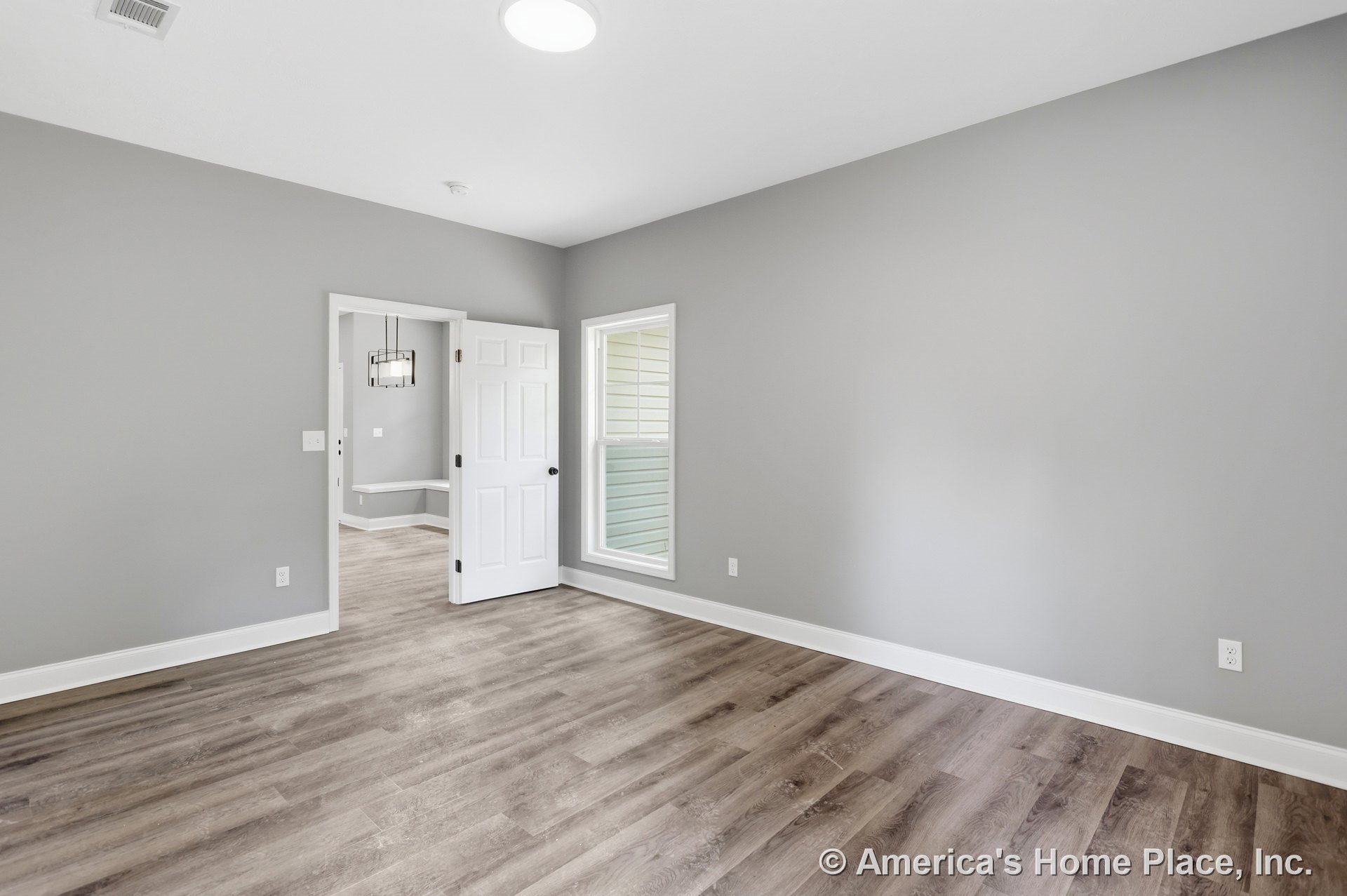 Gray walls with white baseboards and trim, wood-look vinyl plank flooring, single window with white trim, white interior door, recessed ceiling light, empty bedroom with modern