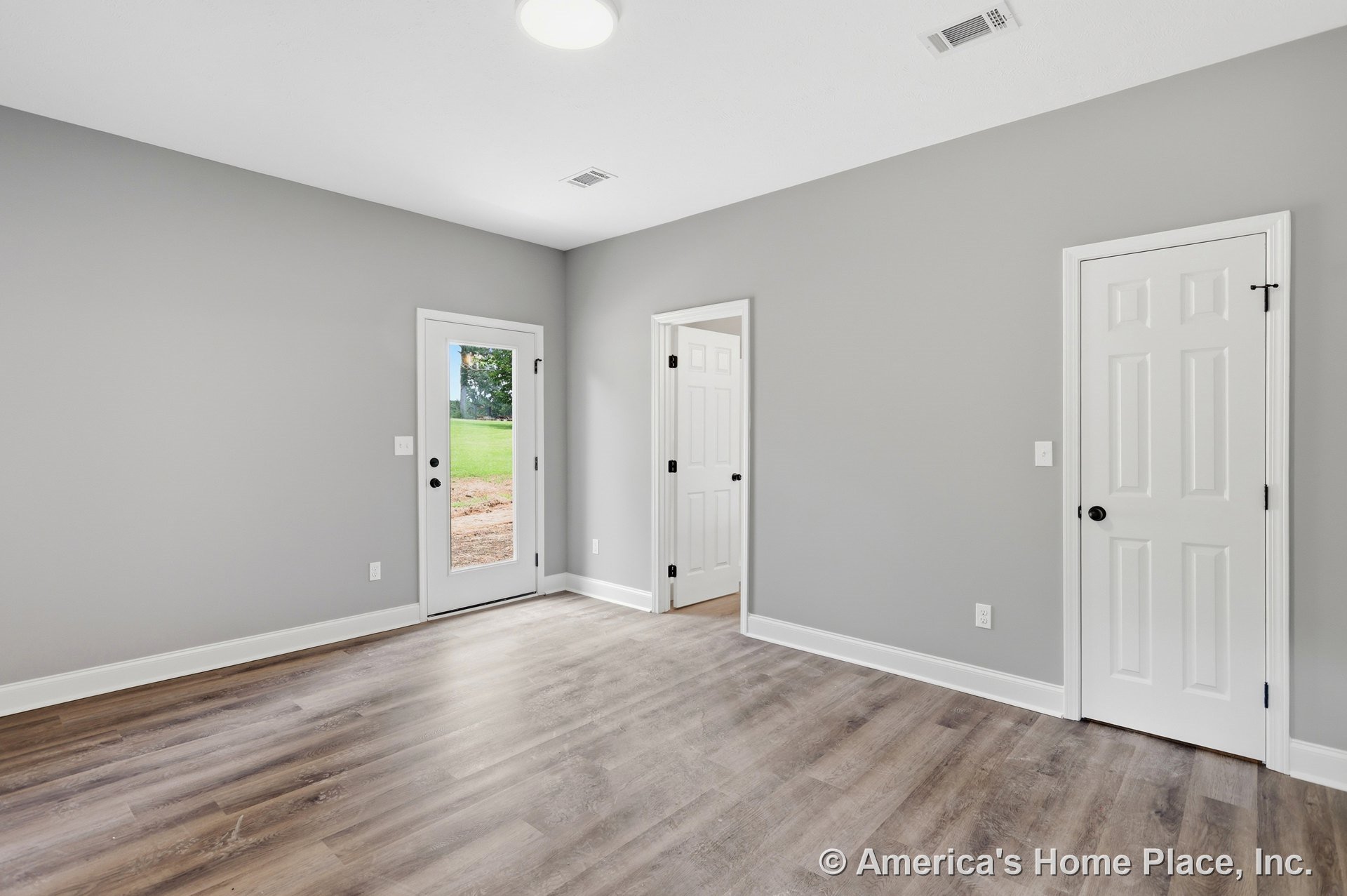Light wood-look vinyl plank flooring, gray painted walls, and white baseboards with three doors including a glass exterior door and two white paneled interior doors; flush ceiling