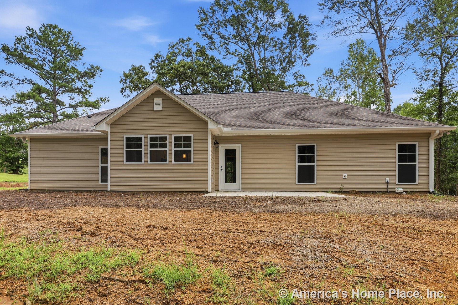 Tan vinyl siding exterior with gable roof clad in asphalt shingles, multiple double-hung windows, concrete entry pad, glass panel exterior door, white trim, outdoor lighting