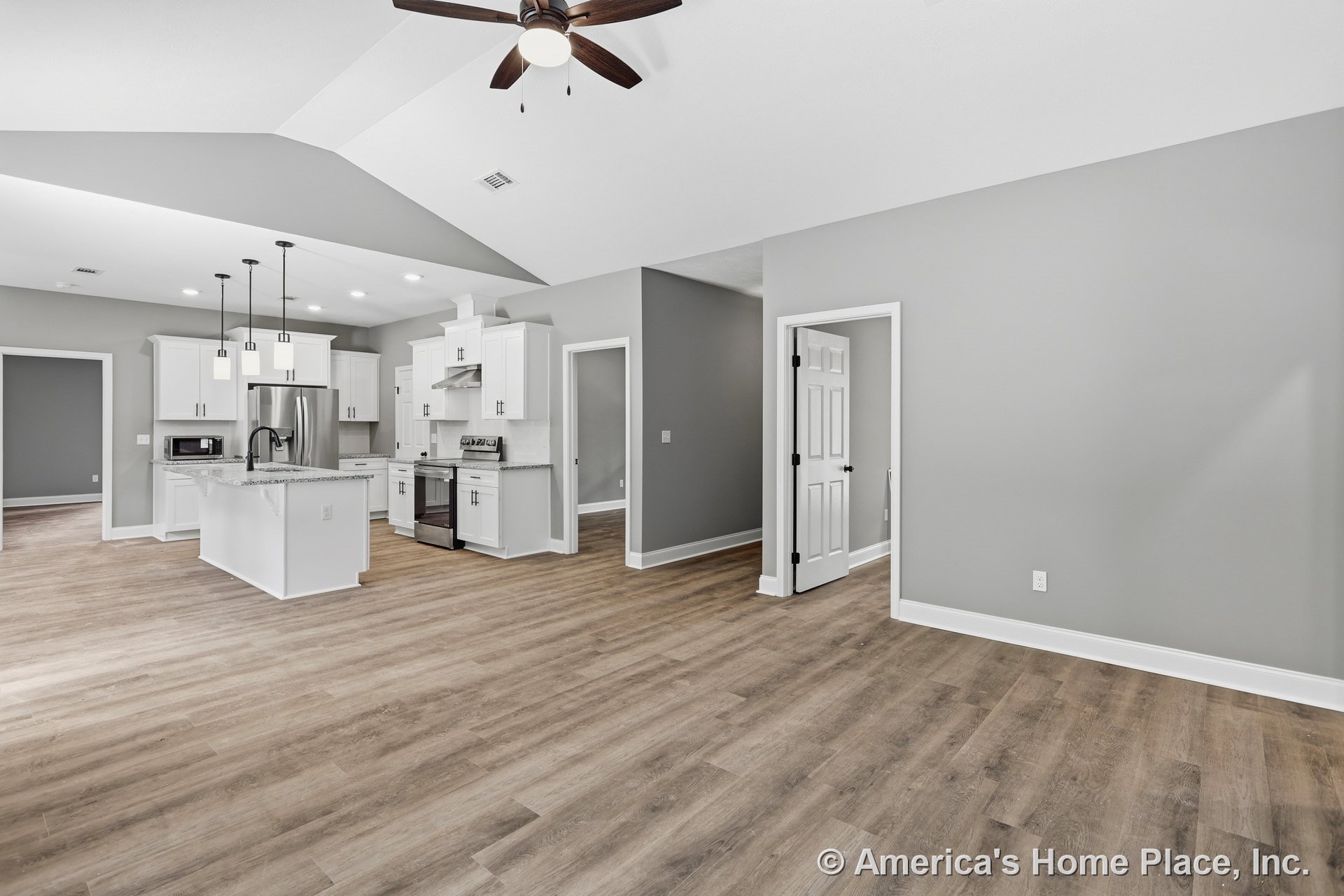 Open kitchen with white cabinetry, granite countertops, stainless steel appliances, vaulted ceiling with ceiling fan, pendant lights above the kitchen island, gray painted walls