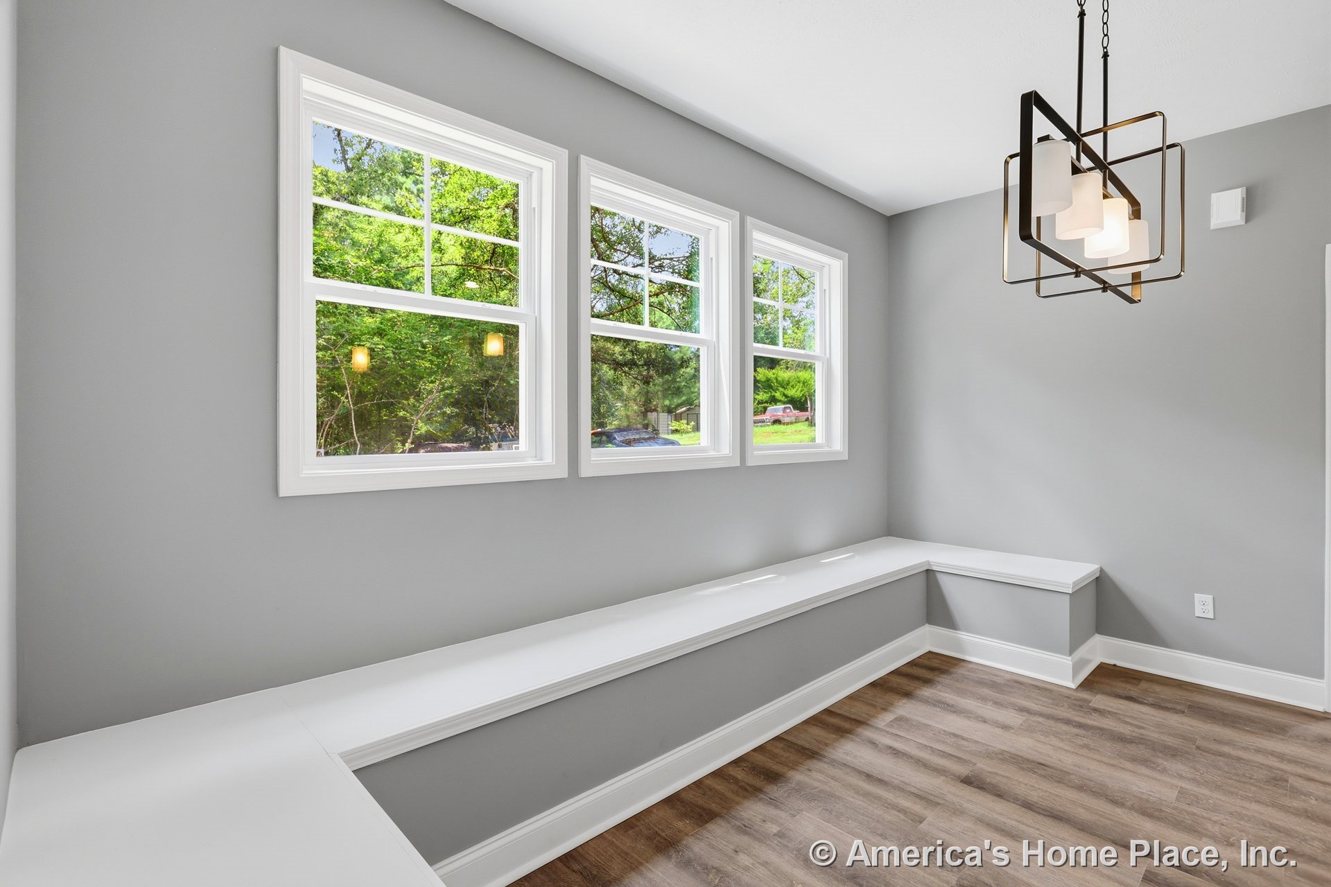 Bright nook with three-pane windows, built-in bench seating, modern geometric pendant light, gray painted walls, white window trim, and wood-look flooring.