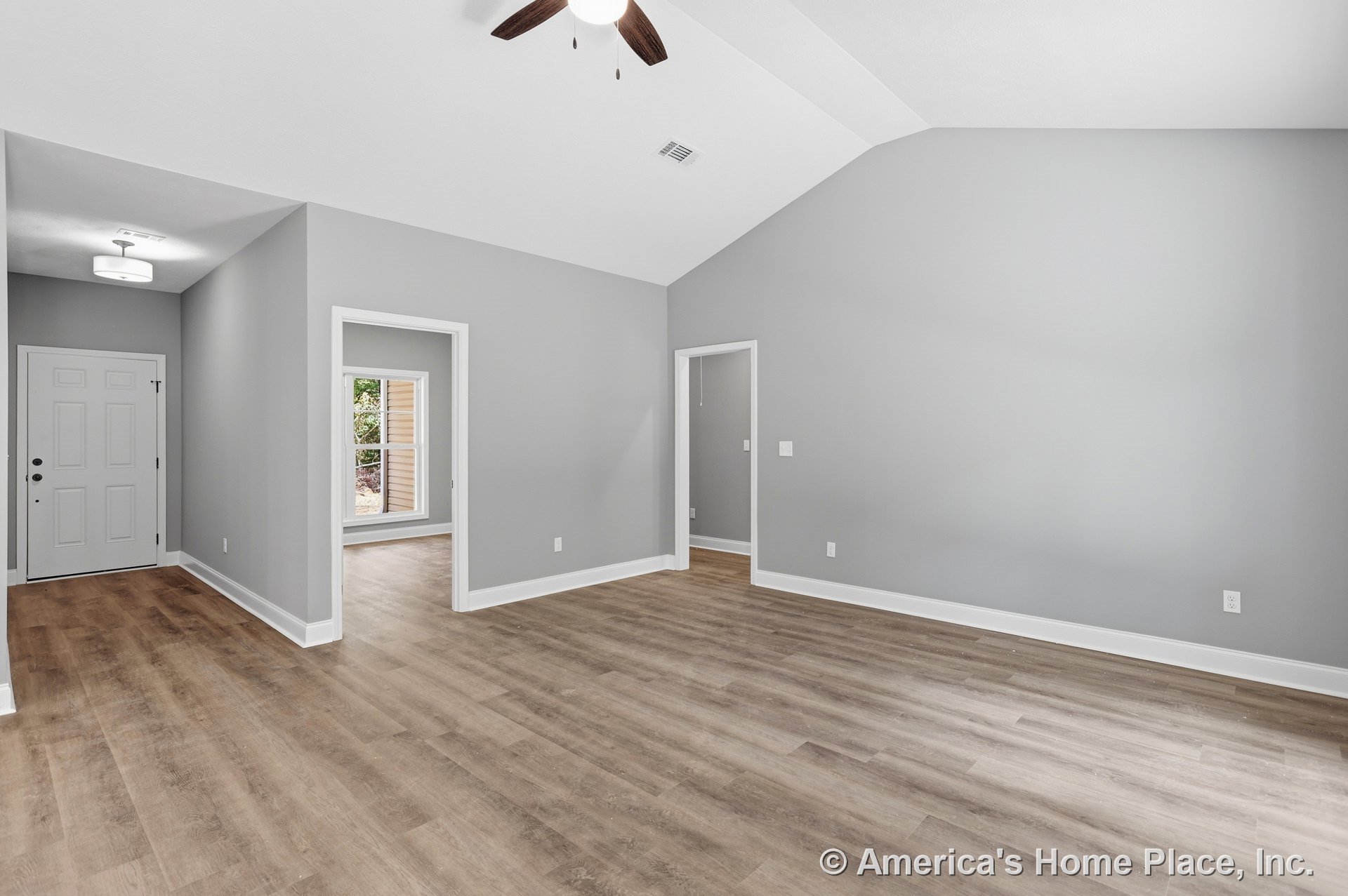 Vaulted ceiling living area with gray painted walls, wood-look plank flooring, white trim and baseboards, entry door with black hardware, ceiling fan, recessed lighting, and open