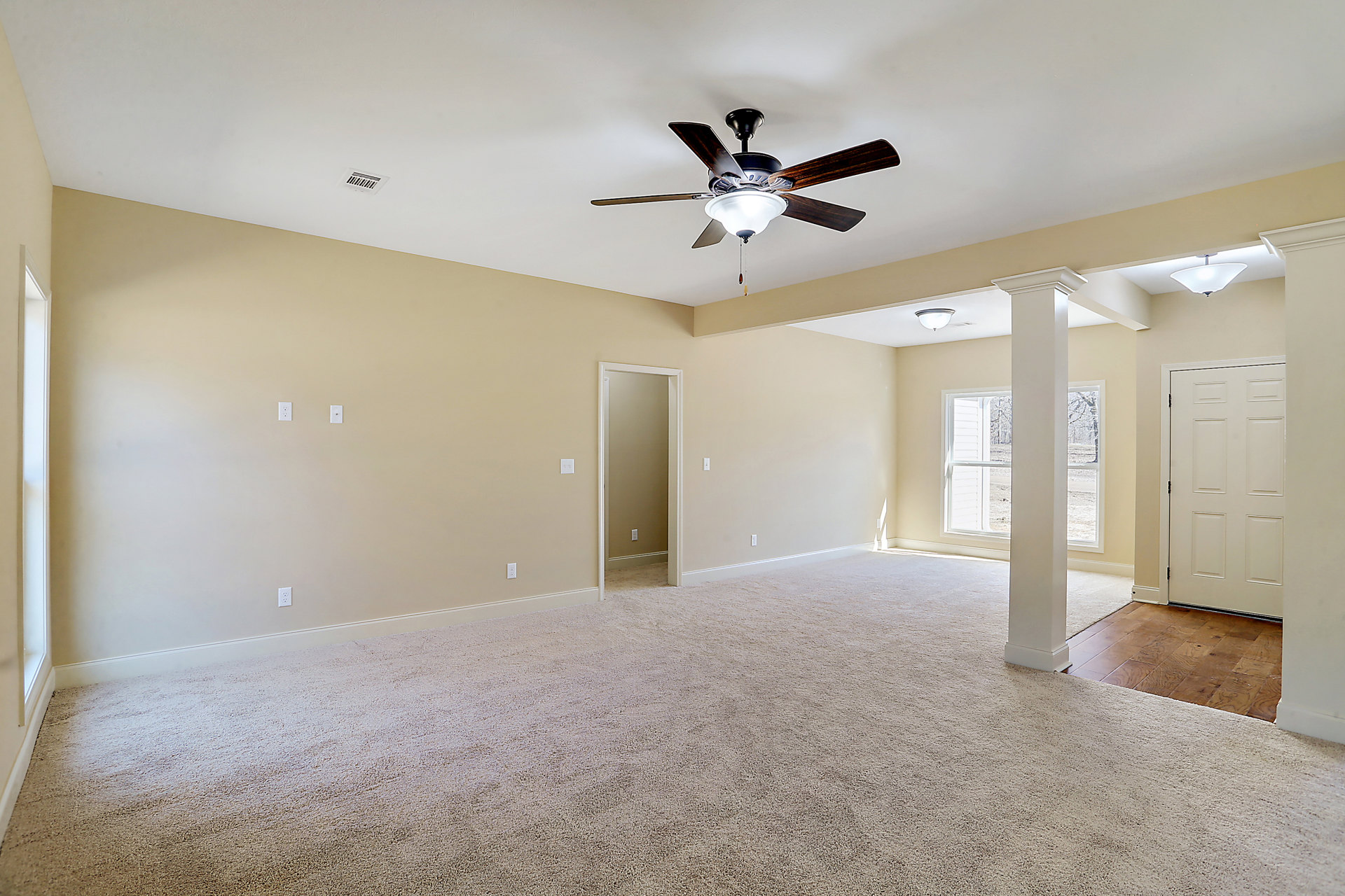 Carpeted room with white walls, ceiling fan with light fixture, white door featuring black handle, and white pillar with metal post