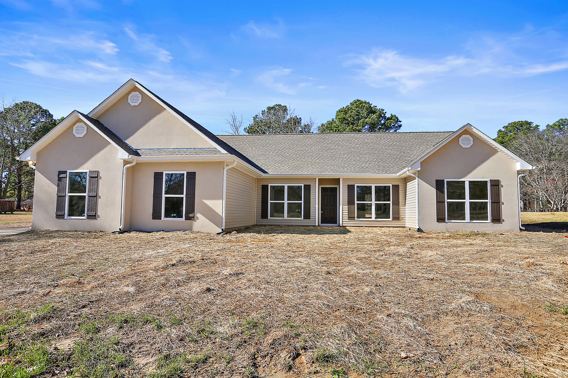 Two-story house with white-framed windows, black front door, gray roof, manicured lawn, mature trees, and blue sky with scattered clouds