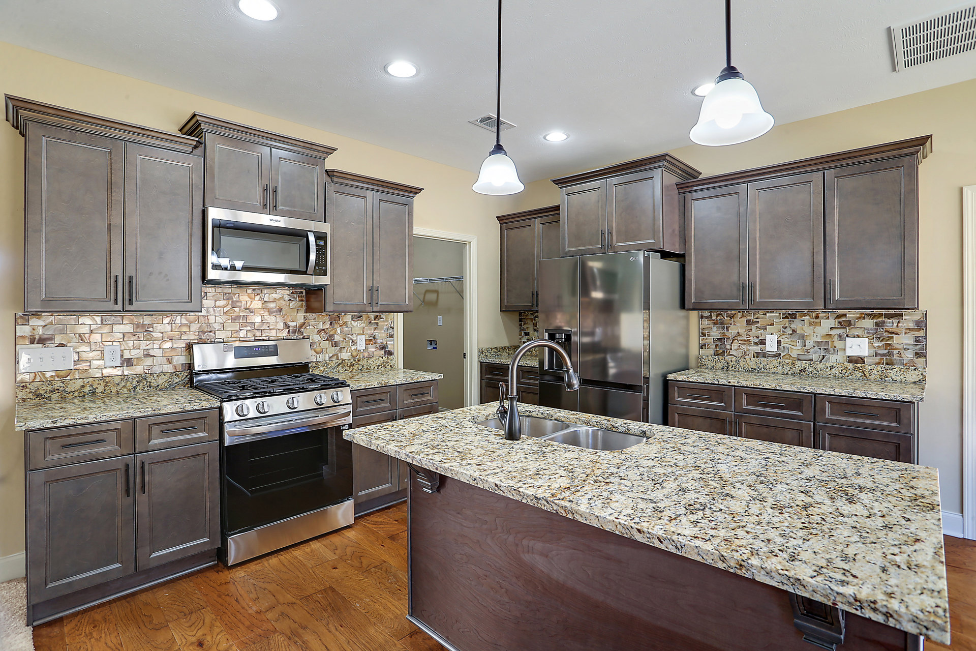 Granite countertops, stainless steel appliances including open oven and glass-door microwave, undermount sink, white cabinetry, ceiling vent, stainless steel refrigerator