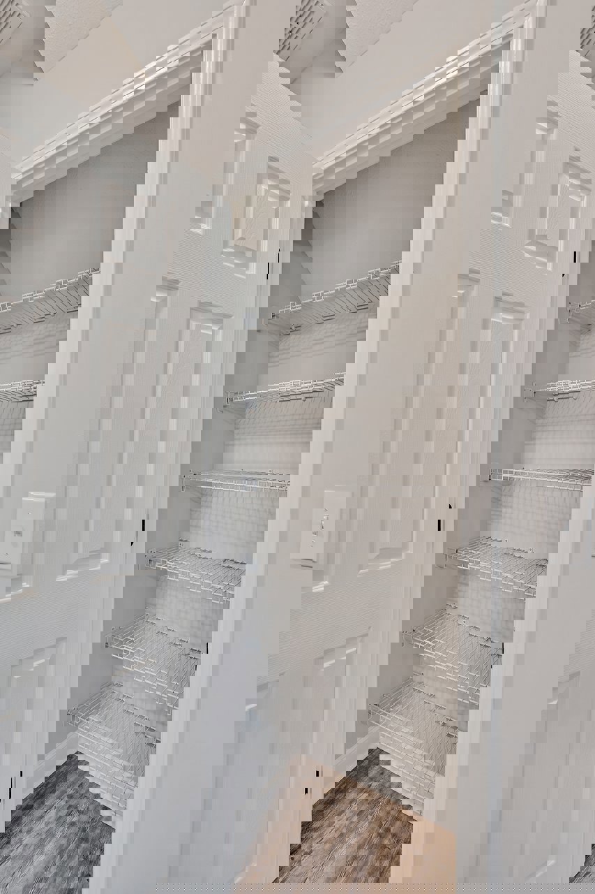 White closet with built-in shelves, wood flooring with wire mesh, white door featuring black handle, light switch on adjacent wall