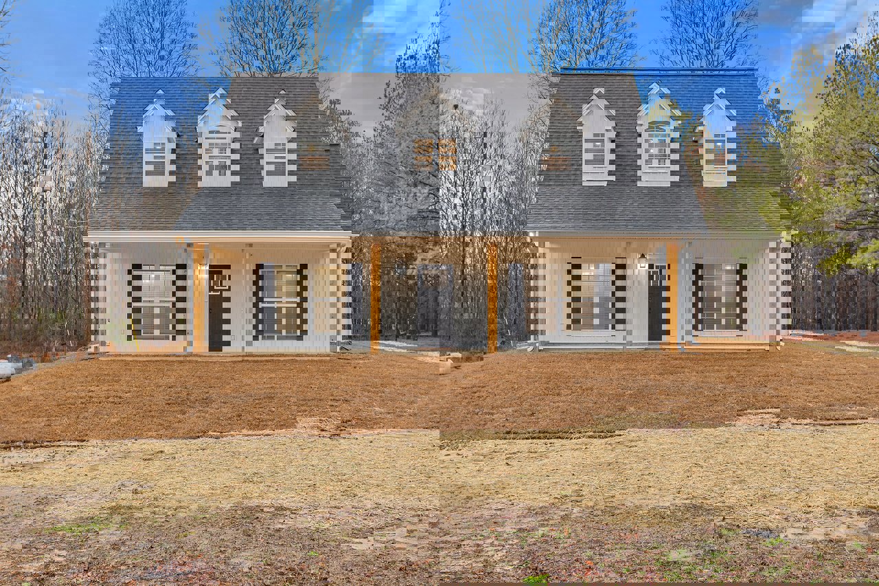 Two-story house with white siding, black-framed windows, black front door, grassy yard, mature trees in background, blue sky overhead